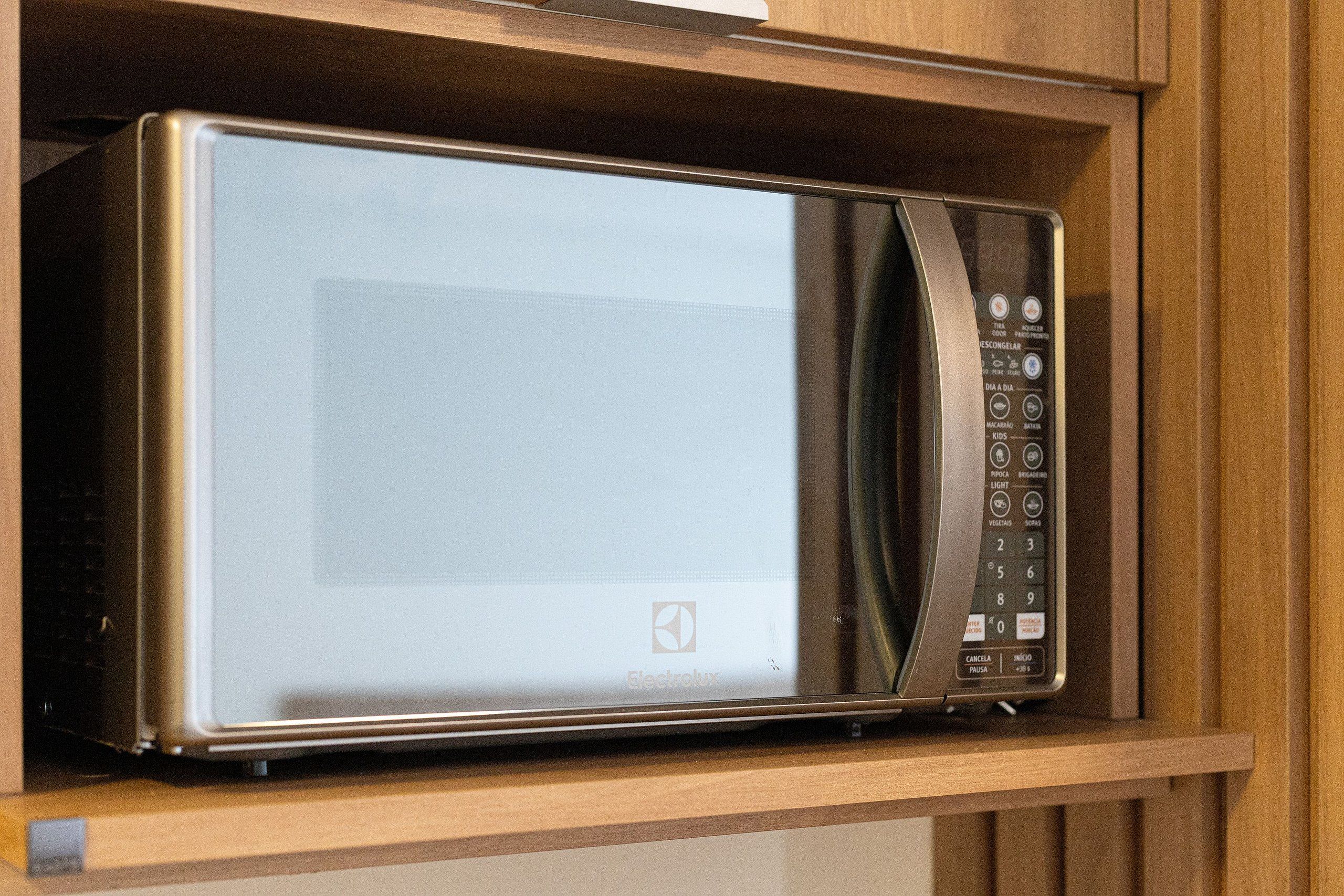 A microwave oven with a digital display and control panel, placed on a wooden shelf.
