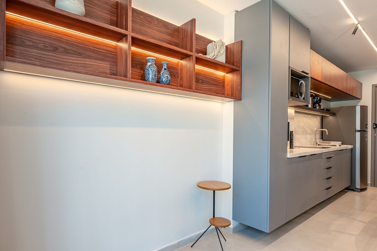 A modern kitchen with built-in wooden shelves, a stainless steel refrigerator, and a round bar stool.