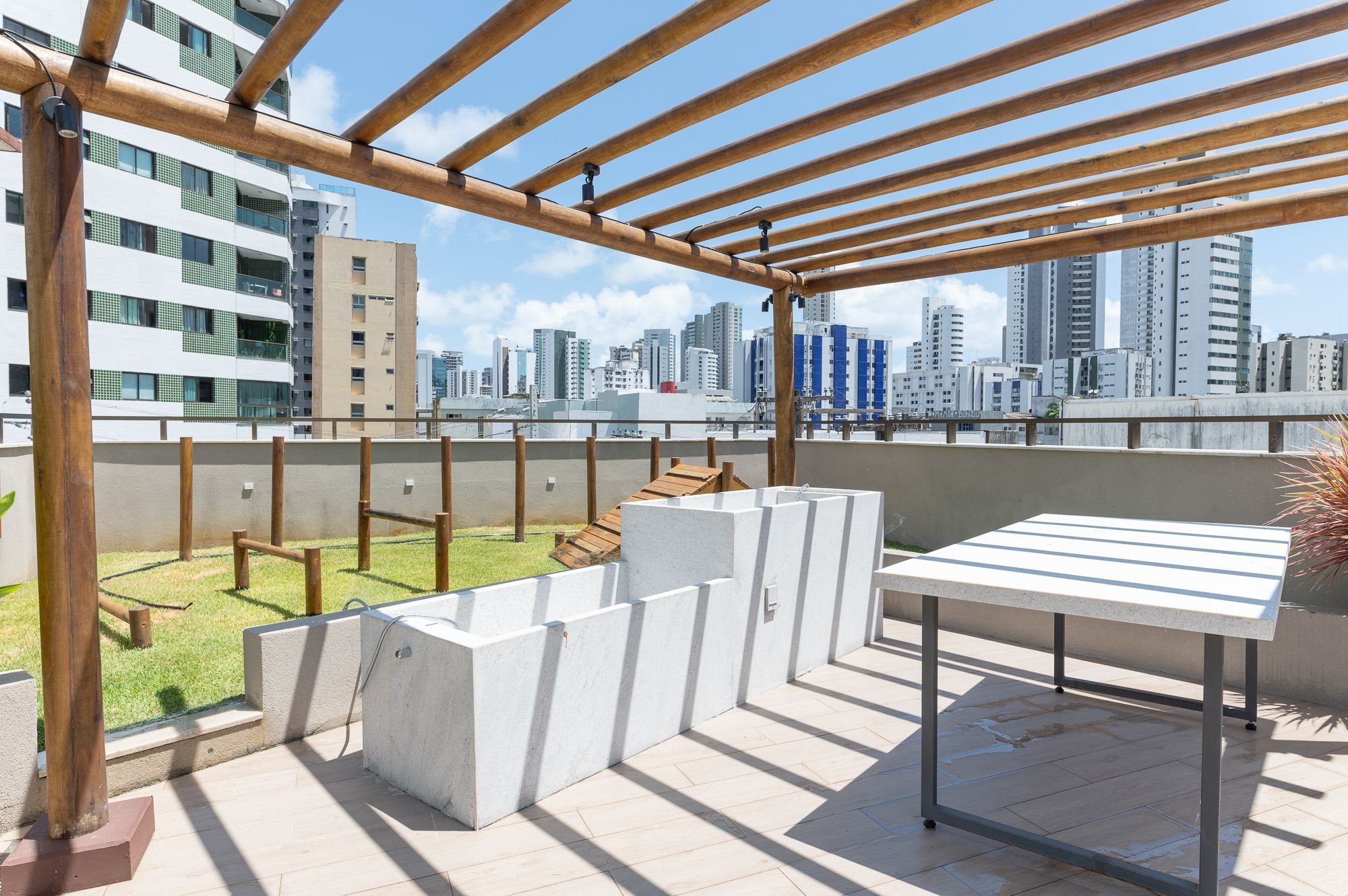 Una terraza en la azotea con una pérgola de madera, un área de descanso de hormigón y vistas al horizonte de la ciudad.