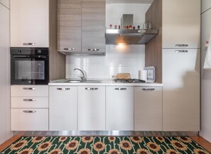 A modern kitchen with white cabinets, a black oven, stainless steel appliances, and a patterned floor mat. - Villa Fior Di Mare - Cala Pira (Cala pira)