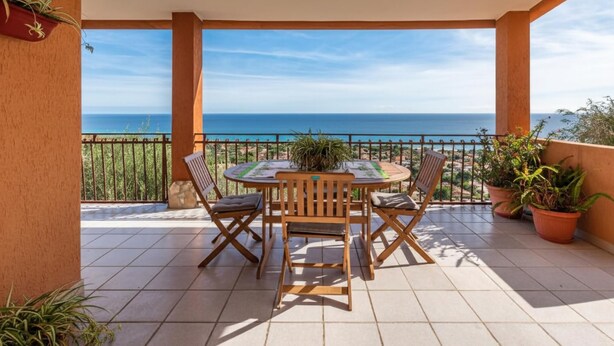 Un portico coperto con tavolo e sedie, piante in vaso e vista sul mare.