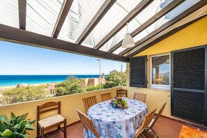 Un porxo cobert amb una taula i cadires, amb vista a una platja i l'oceà.