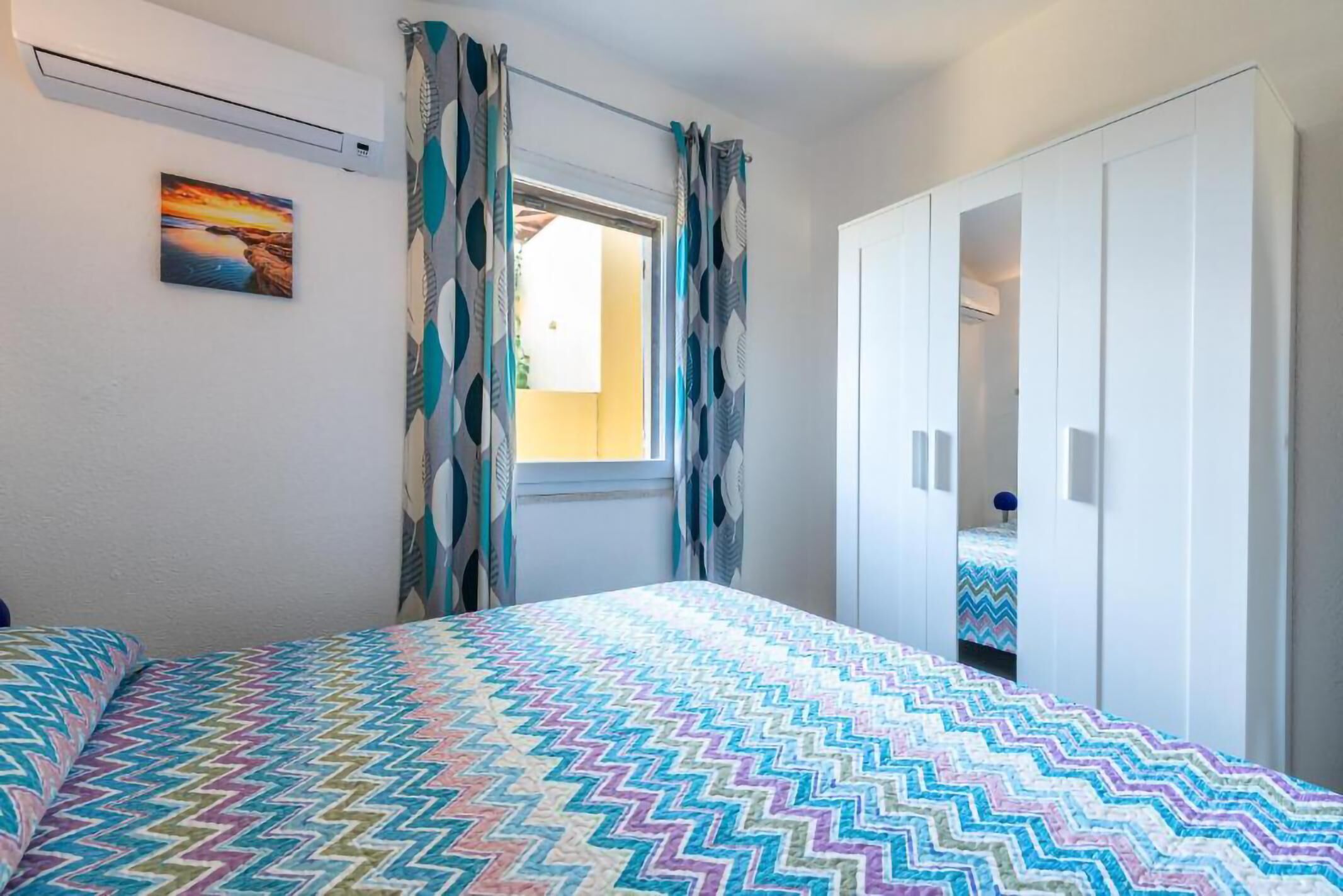 Une chambre à coucher avec un lit, une fenêtre avec des rideaux, une armoire et un tableau au mur.