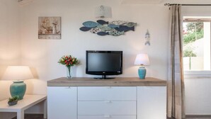 Ein modernes Wohnzimmer mit einem Flachbildfernseher auf einer Holzkonsole, einer Blumenvase, einer Lampe und Kunstwerken an den Wänden.