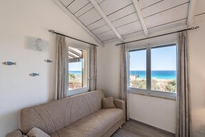 Ein Zimmer mit einem beigen Sofa, einer Decke mit Holzbalken und zwei mit Vorhängen versehenen Fenstern.