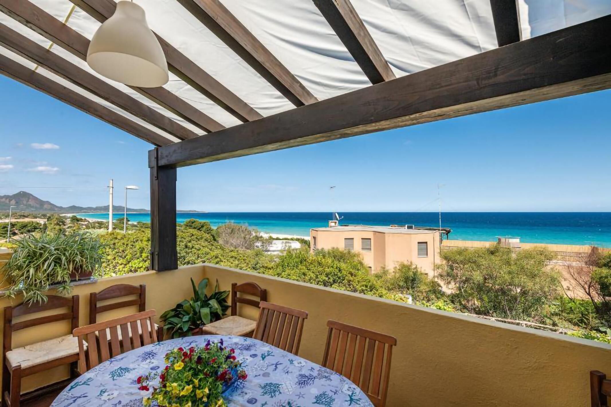 A covered outdoor seating area with a table and chairs, overlooking a beach and ocean.