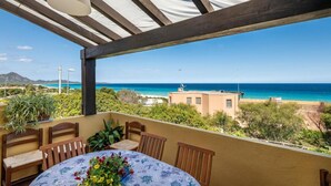 Ein überdachter Außenbereich mit Tisch und Stühlen, mit Blick auf einen Strand und das Meer.
