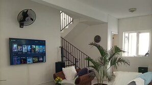 Un soggiorno con mobili in vimini, una televisione a parete, una pianta in vaso e una scala.