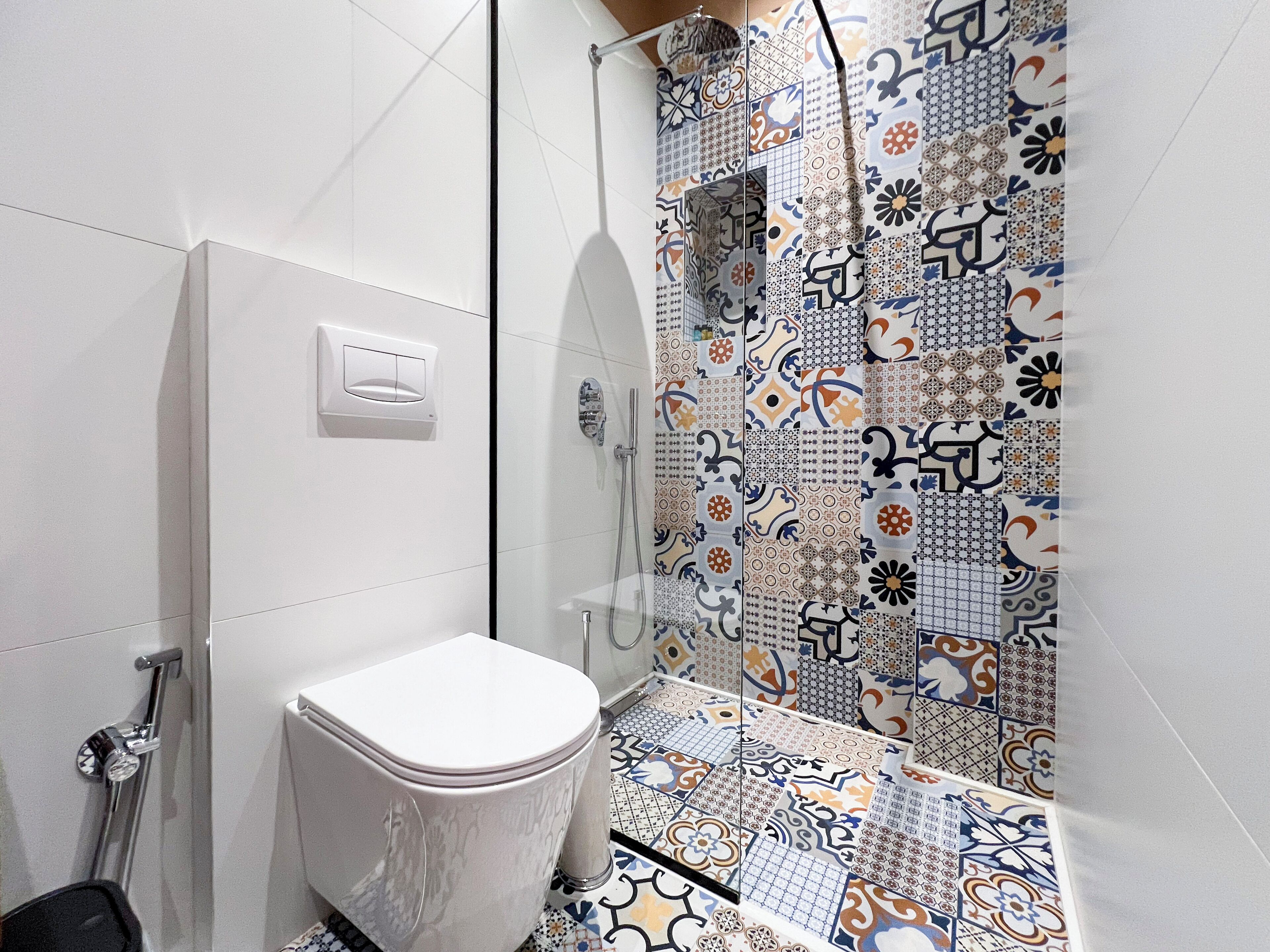 A bathroom with a white toilet, a shower with a glass door, and a tiled floor with a variety of patterns.