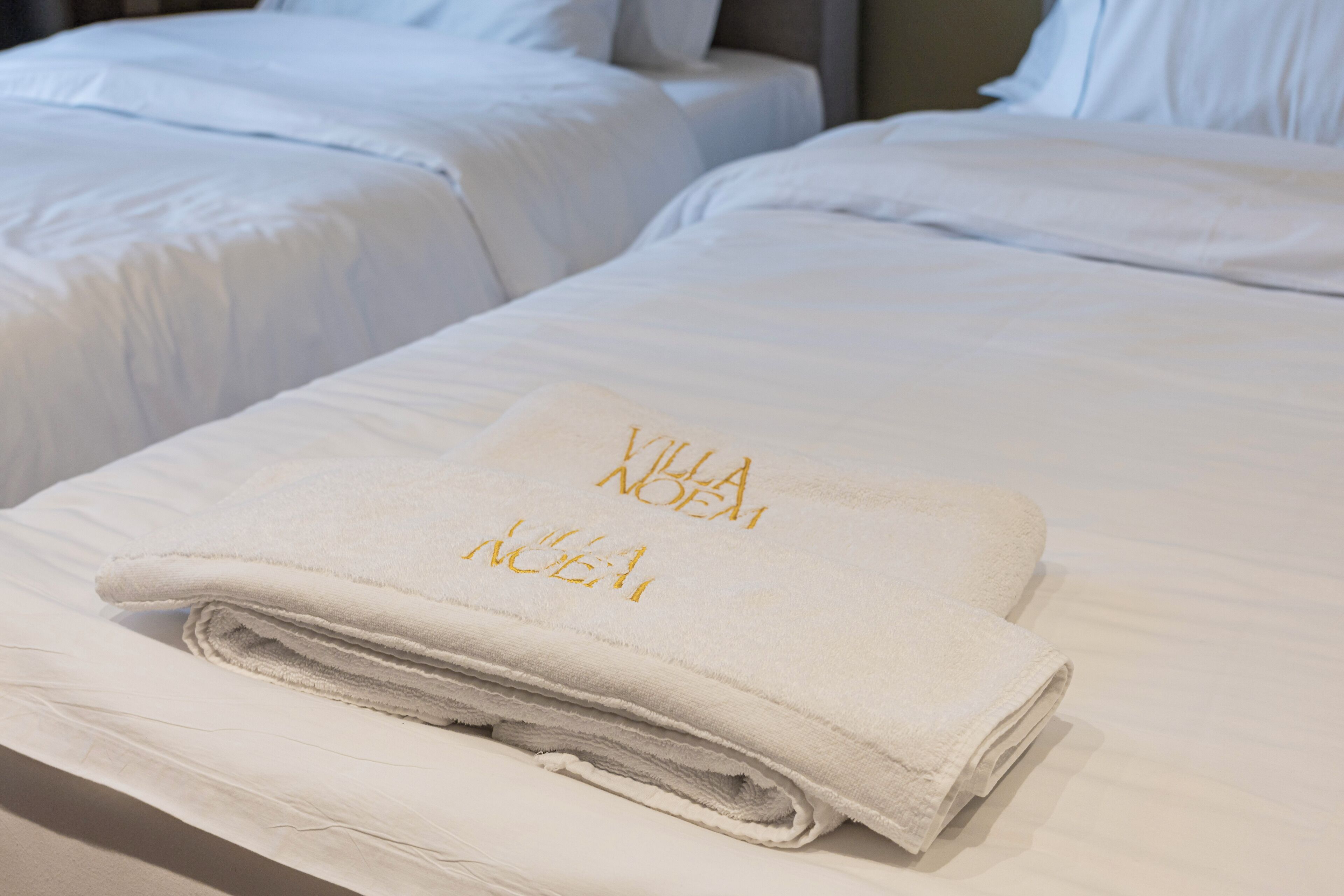 A neatly made bed with a folded towel on top, and two beds in the background.