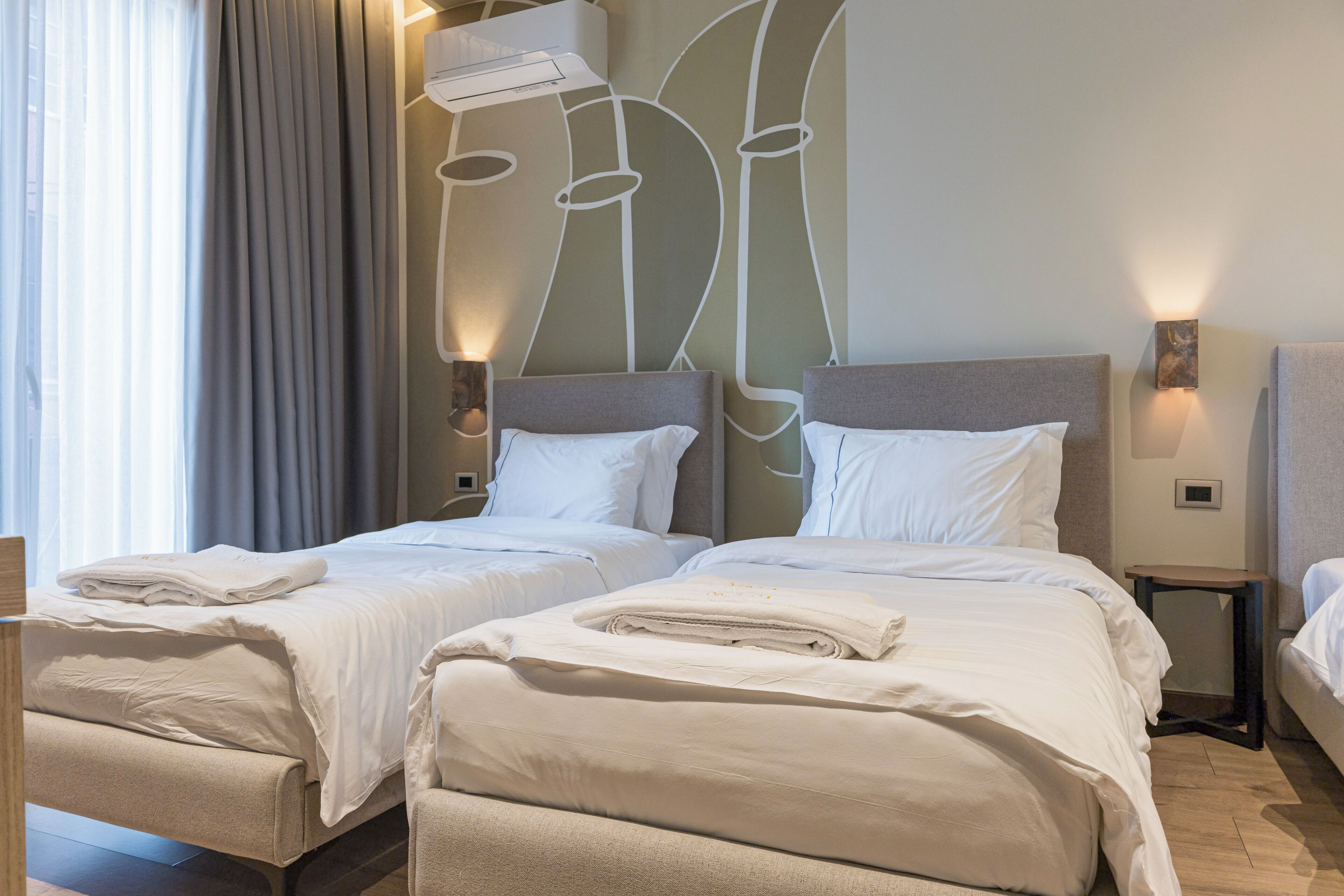 Habitación de hotel con dos camas, cada una con sábanas y almohadas blancas, un diseño moderno en la pared y un ventilador de techo.