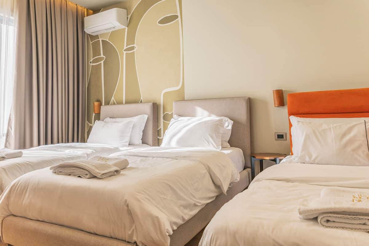 Una habitación de hotel con dos camas, ropa de cama color beige, un diseño moderno en la pared y un equipo de aire acondicionado.