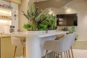A modern kitchen with a white countertop, two chairs, and a variety of plants. - Villa Noem (Tirana)