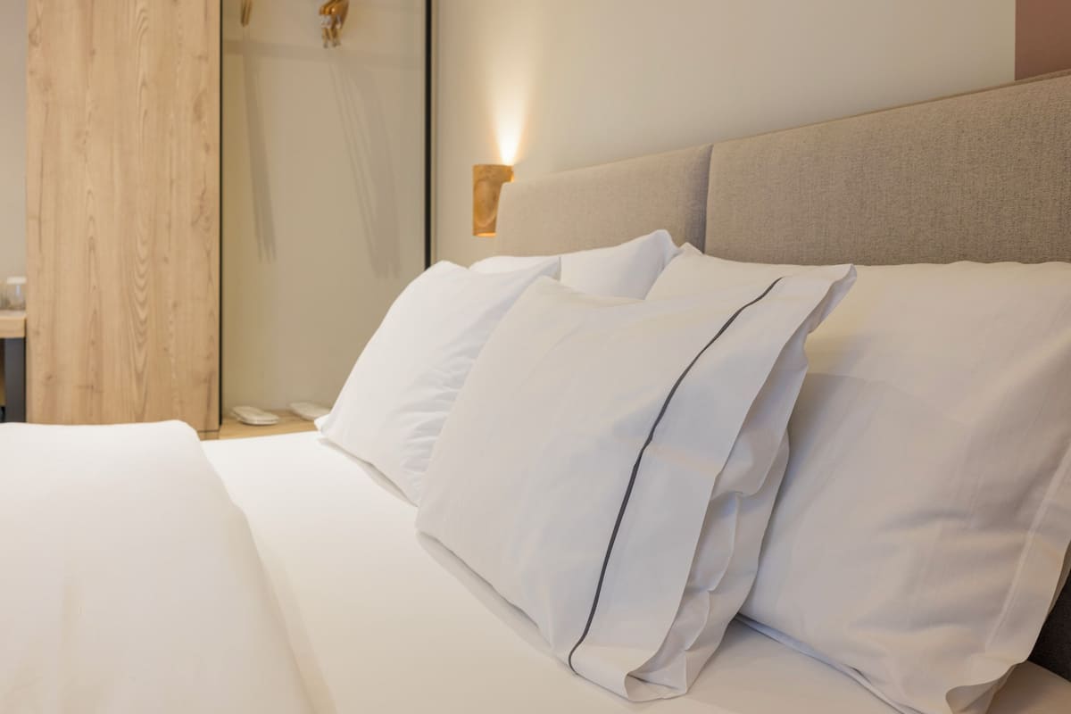 Una cama bien hecha con sábanas blancas y un cabecero de tela clara.