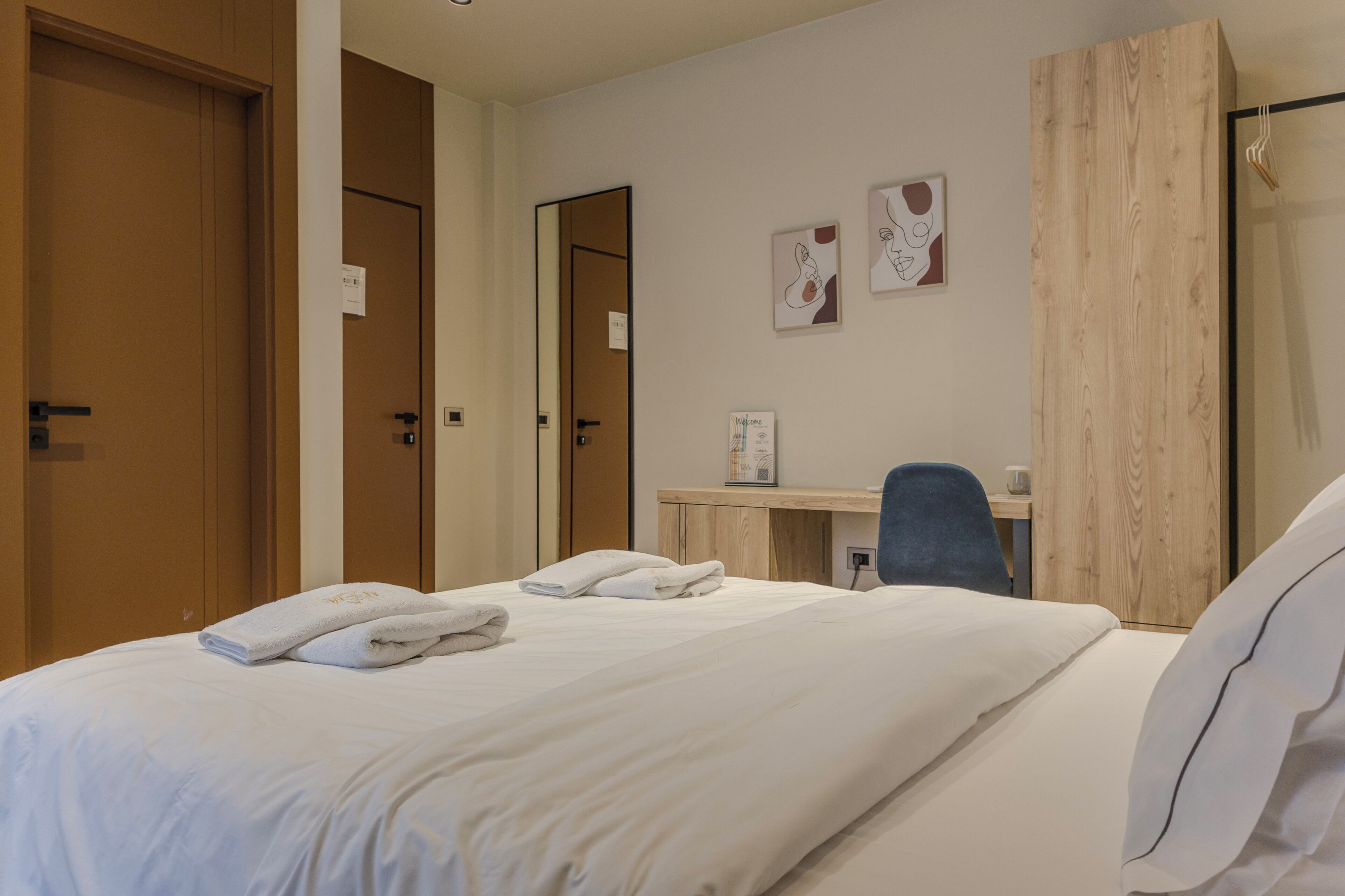 A hotel room with a neatly made bed, a desk with a chair, and a wardrobe.