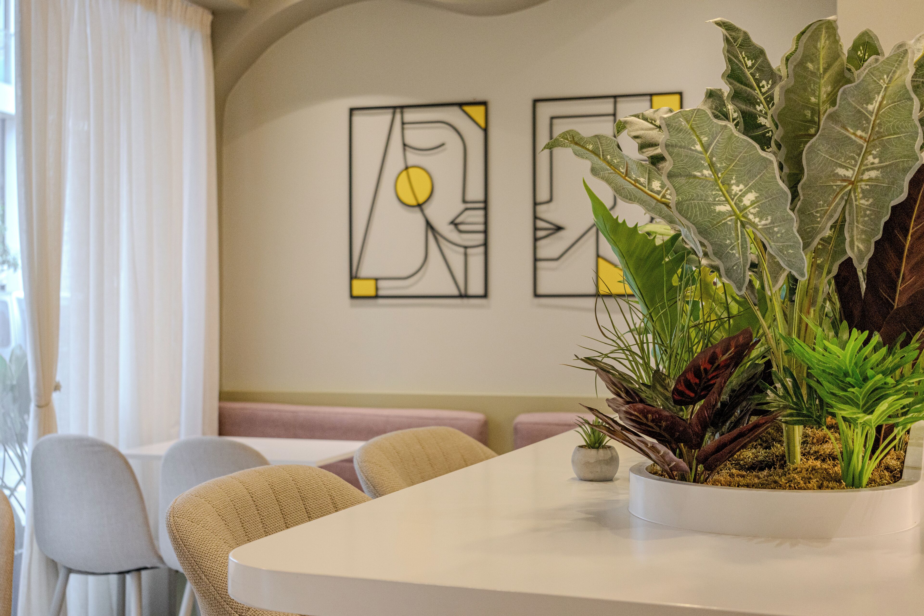 A modern dining area with a white table, beige chairs, and a potted plant.