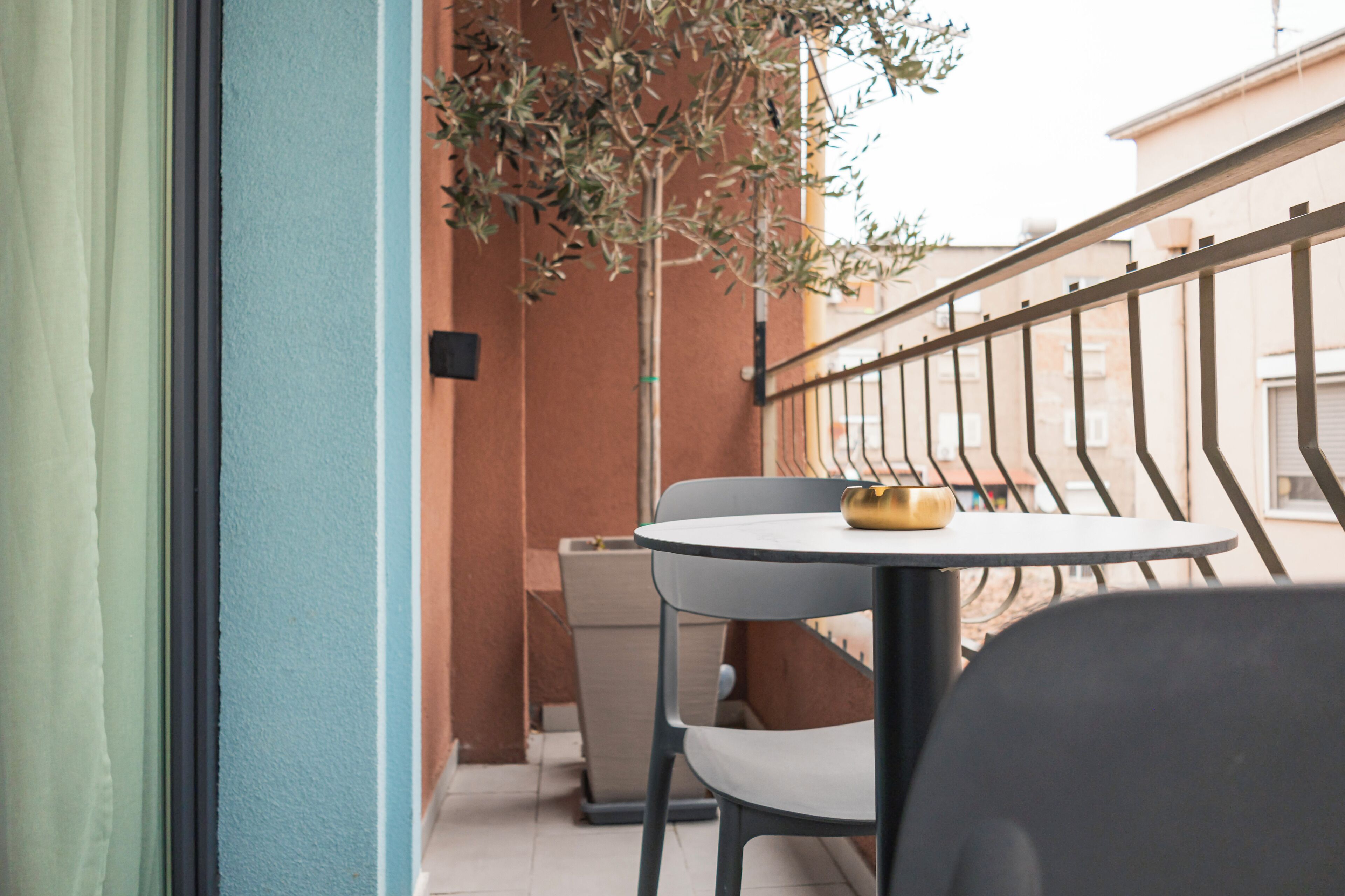 Un balcon avec une table ronde et deux chaises, une petite plante et une poubelle.