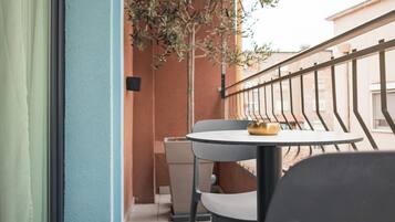 Un balcon avec une table ronde et deux chaises, une petite plante et une poubelle.