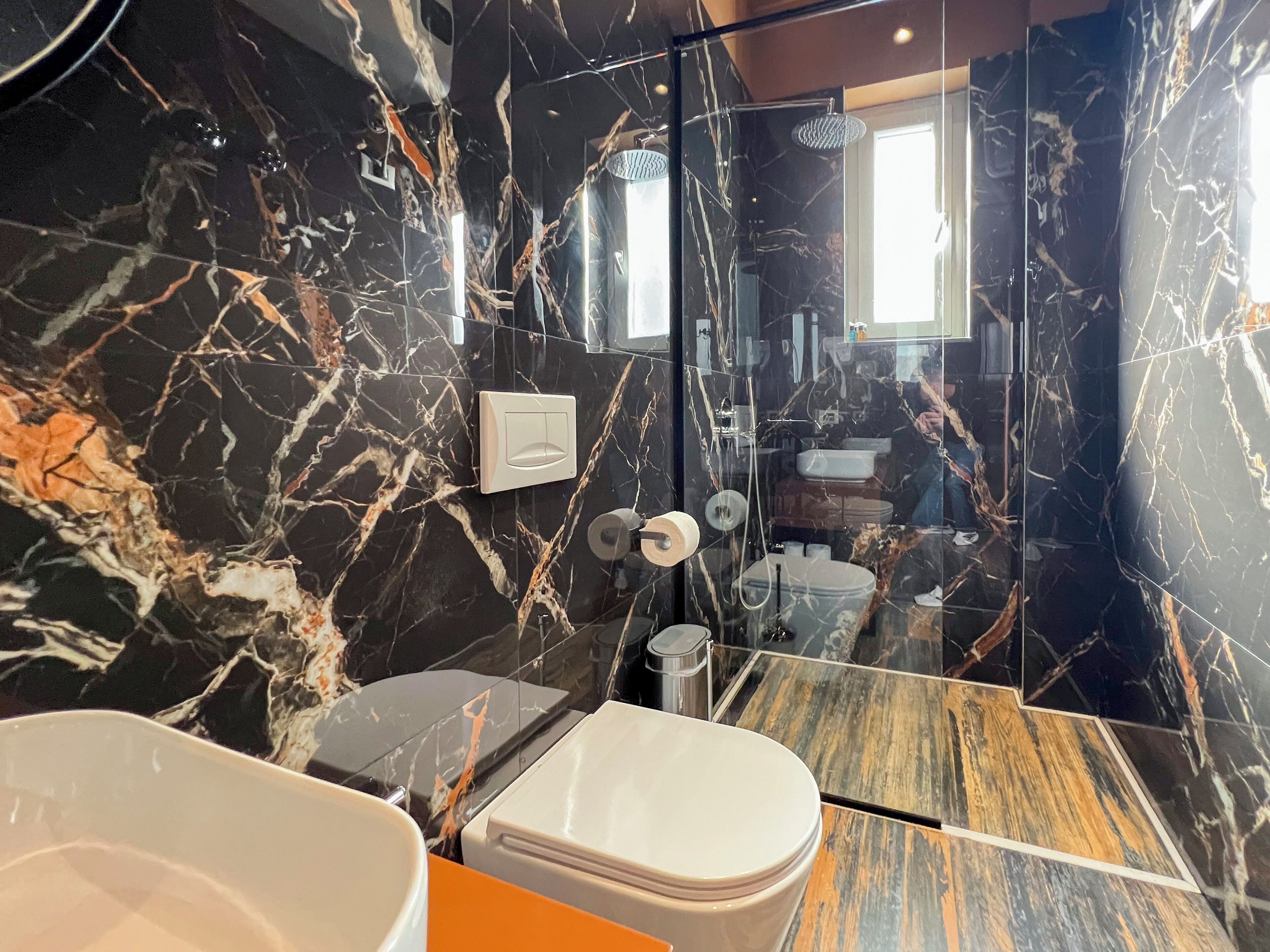 A bathroom with a marble wall, a toilet, a sink, and a shower.