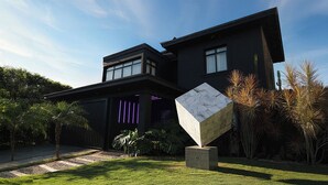 A modern two-story house with a dark exterior, a visible window, and a unique geometric sculpture in the front yard. - Artistic Dream Mansion in Jurere International, Brazil (Florianópolis)