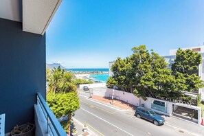 A coastal view from a balcony overlooking a street with a parked car, a building labeled 'The Clifton,' and a clear blue sky. - Clifton Escape - Stylish Studio near beach by ctha (Cape Town)