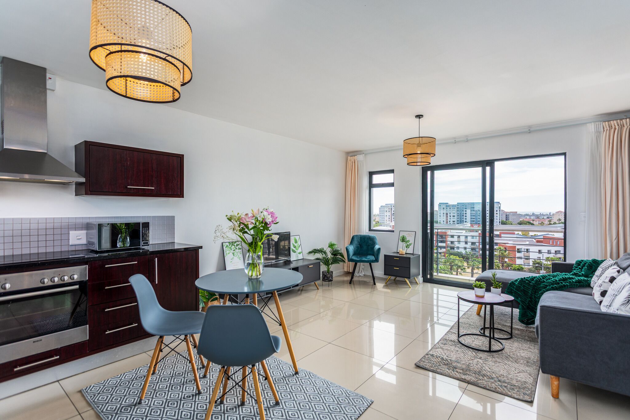 Een modern appartement met een keuken, eethoek en woonkamer. Het heeft een groot raam met uitzicht op de stad, een eettafel met stoelen en een bank.