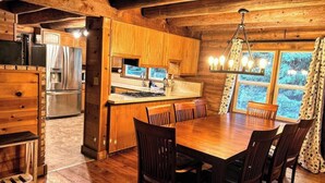 Ein Holzblockhaus-Interieur mit Essbereich, Küche und einem großen Fenster mit Vorhängen.