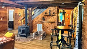 Ein gemütliches Blockhaus-Interieur mit Kaminofen, Essbereich und einer Treppe, die zu einer oberen Ebene führt.