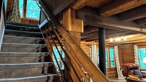 Eine Holztreppe mit Geländer führt zu einem Raum mit einem Ledersessel und einem Tisch.