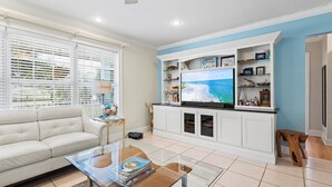 A living room with a white sofa, a glass coffee table, and a flat-screen TV on a white entertainment unit. - Lakehouse with Sunsets, Private Pool and Jacuzzi, 1Mi to Indian River Lagoon (Sebastian)