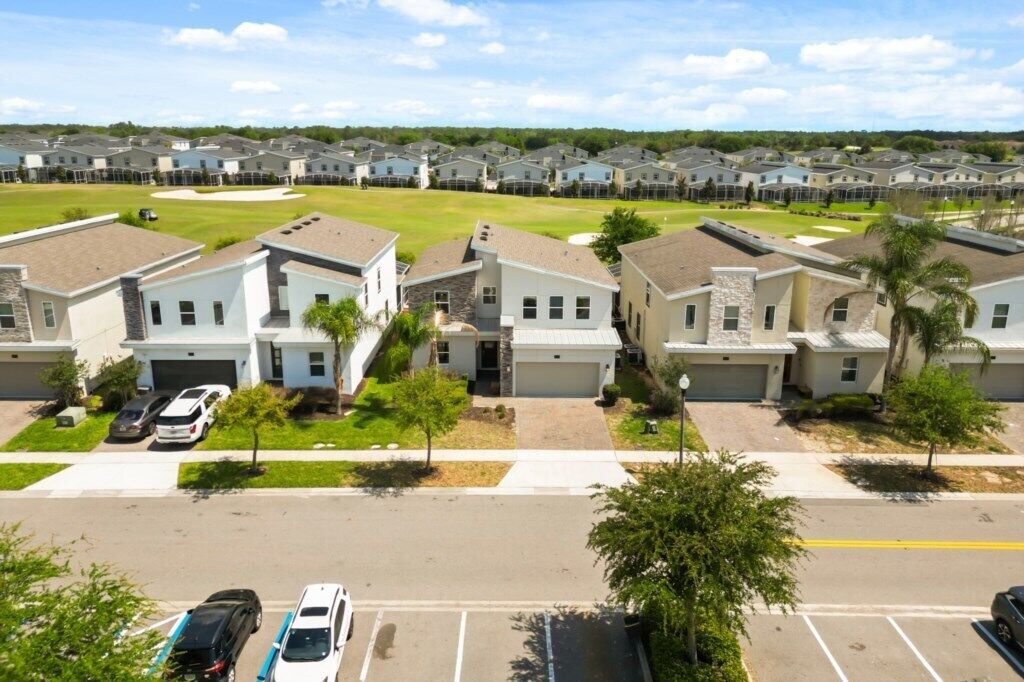 A residential community with single-family homes, a parking lot, and a green field.