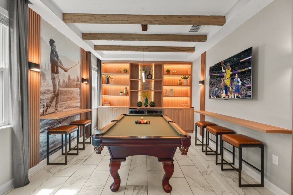 A pool table with stools, a mural, shelves with decorative items, and a TV on the wall.