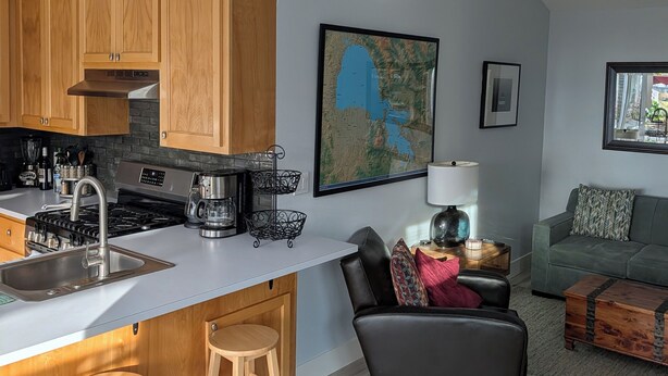Une cuisine moderne avec des meubles en bois, un grand îlot central doté de tabourets, un coin repas avec un canapé et une table basse, et un ventilateur de plafond.
