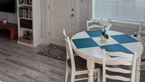 Un coin repas avec une table ronde, des chaises blanches et un chemin de table à carreaux bleus et blancs.