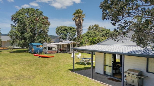 A spacious outdoor area with a covered seating area, a barbecue grill, and a trailer. - Golden Sands Retreat - Matarangi Holiday Home (Matarangi)