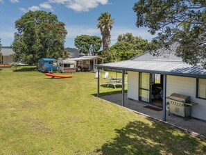 Un vaste espace extérieur comprenant un coin salon abrité, un barbecue et une remorque.