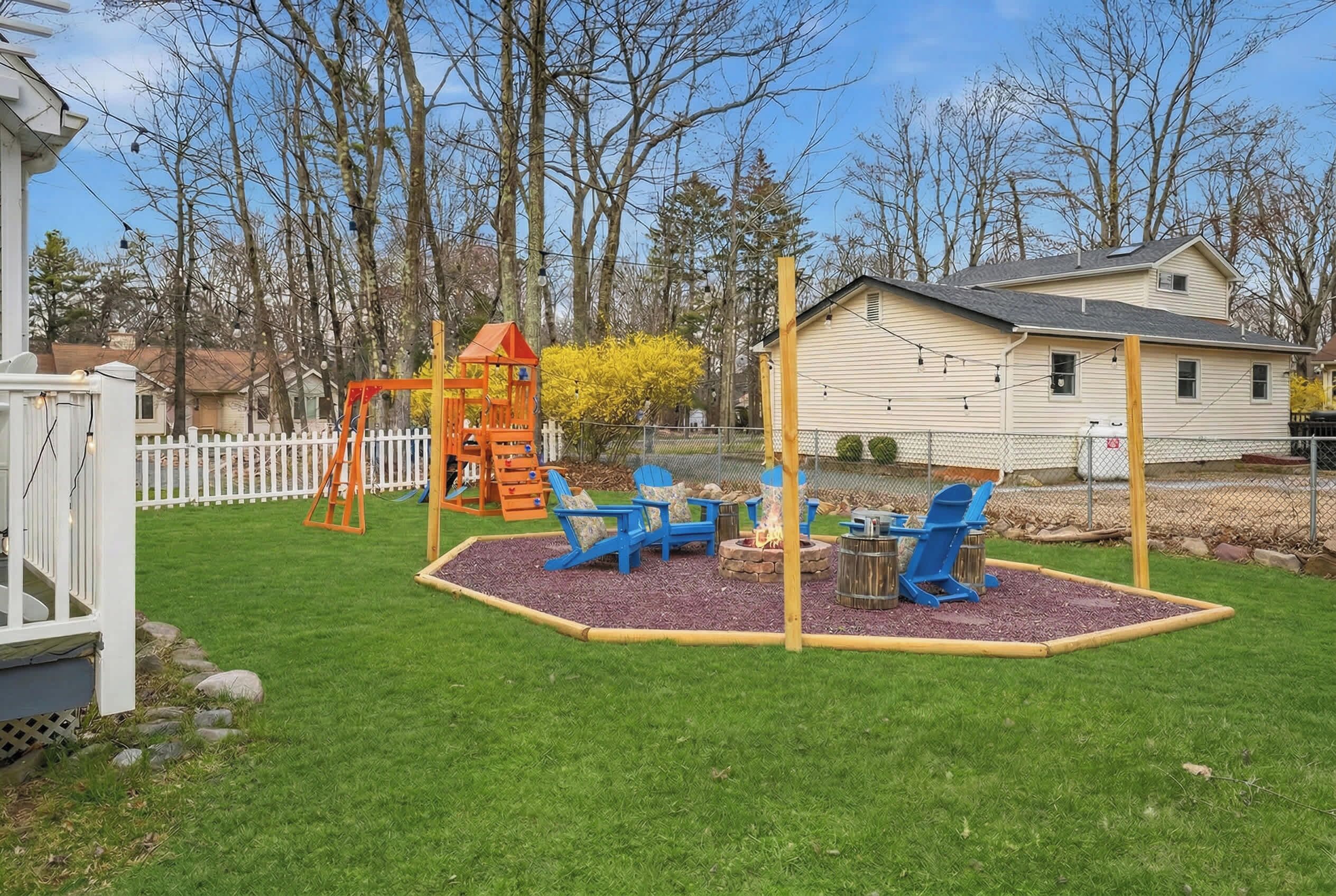 Un patio trasero con un columpio, sillas azules y una chimenea.