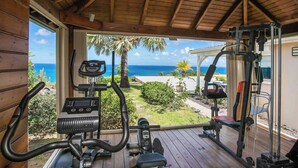 Ein Freiluft-Fitnessbereich mit Trainingsgeräten, mit Blick auf einen Strand und Palmen.