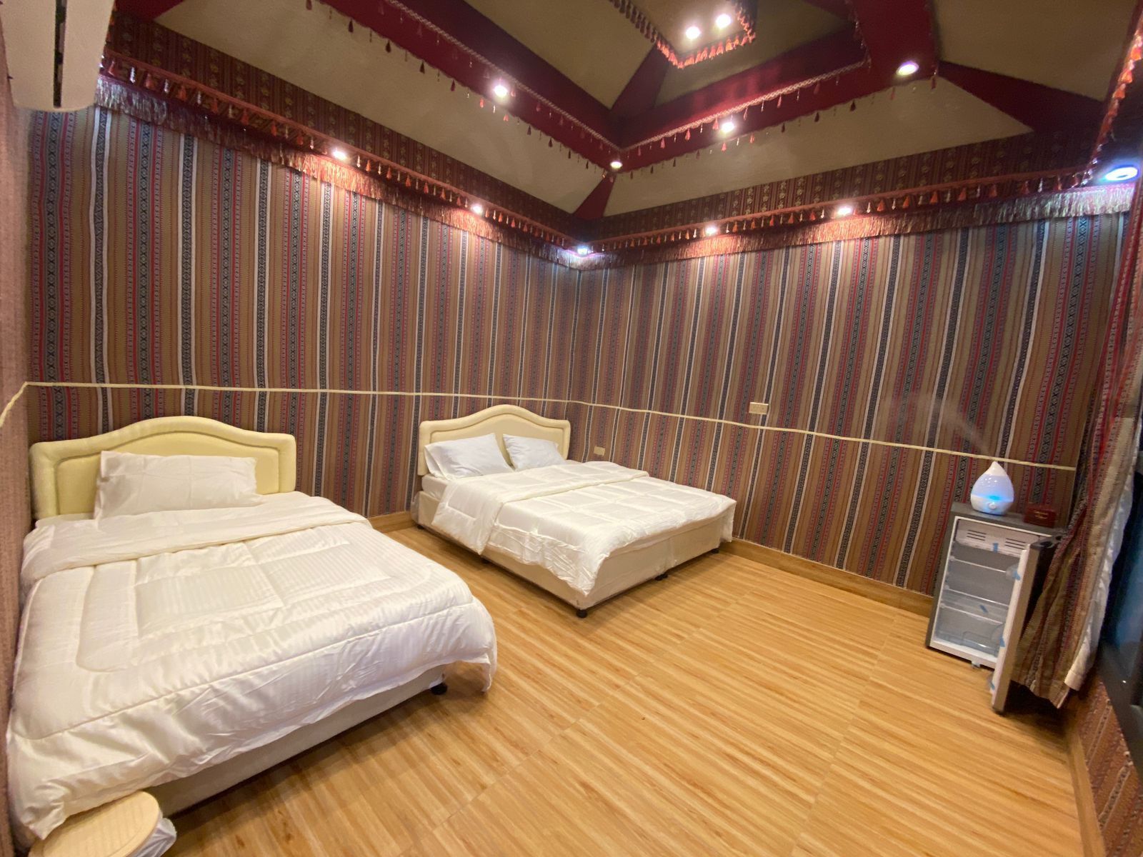 Habitación con dos camas, piso de madera y papel tapiz a rayas.