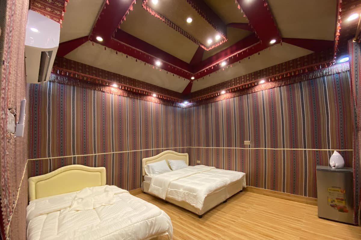 A hotel room with two beds, wooden flooring, patterned curtains, and a ceiling with exposed beams and lights.