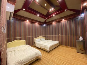Ein Hotelzimmer mit zwei Betten, Holzboden, gemusterten Vorhängen und einer Decke mit freiliegenden Balken und Lampen.