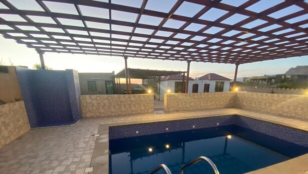 An outdoor swimming pool with a pergola overhead, surrounded by stone walls and a tiled floor. - Sun Horizon Chalet (Nizwa)
