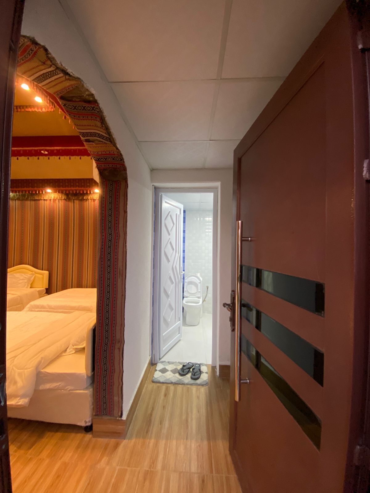 Una habitación de hotel con cama, puerta que da a un baño y piso de madera.