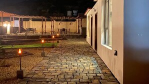 A stone-paved outdoor area with a pergola and seating, leading to a building with a white exterior and a window. - Sun Horizon Chalet (Nizwa)