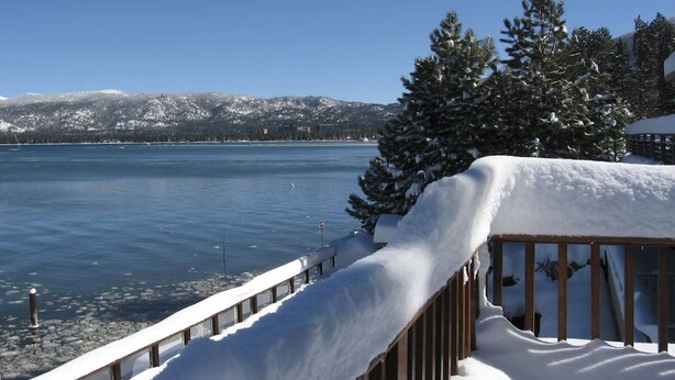 Um deck coberto de neve com vista para um lago e montanhas ao fundo.