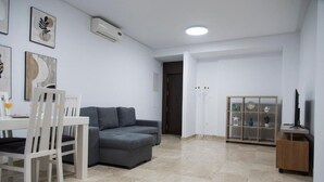 A modern living room with a grey sofa, white chairs, a dining table, and a decorative shelf. - Night In Sevilla Duplex (Seville)