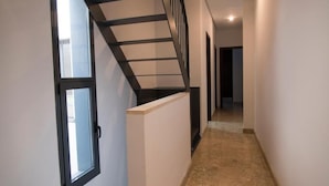 A narrow hallway with a staircase on the left, leading to a door with a window. The walls are plain, and the floor is tiled. - Night In Sevilla Duplex (Seville)