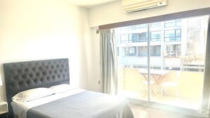 A hotel room with a large bed, an air conditioner, and a balcony with a table and chairs.