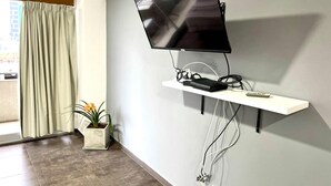 A modern room with a mounted TV on a white shelf, a potted plant, and a window with curtains.