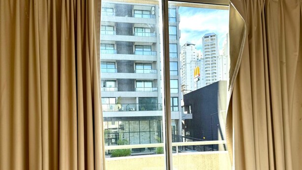 A view from a window with beige curtains, overlooking a building with multiple floors and balconies. - Alassio apartment, Pile view (Buenos Aires)